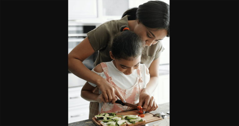 parent helping child cut vegetables