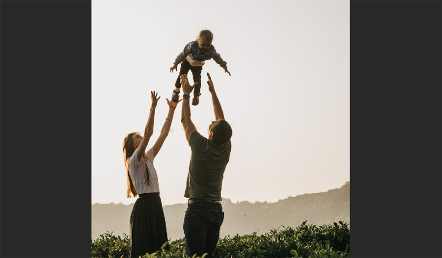 mom and dad in field tossing child in air