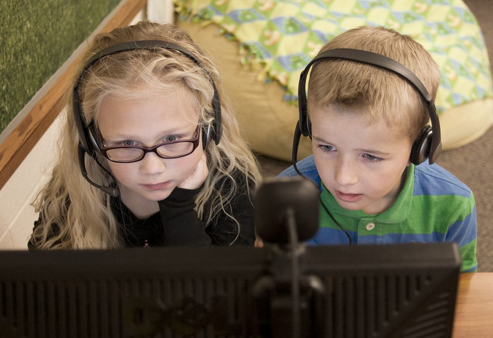 two children wearing headsets sitting in front of a computer