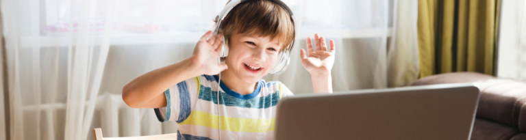 young boy smiling and waving wearing white headphones in online class
