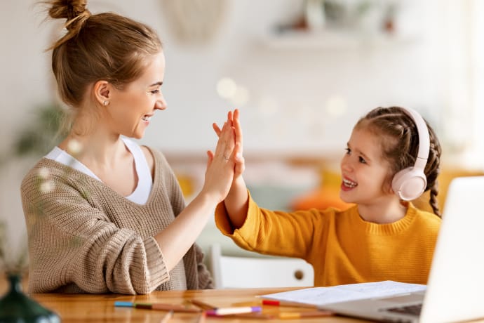 mother giving young young daughter a high-five during online lesson