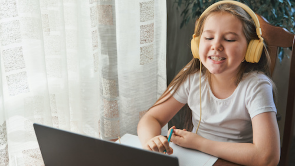 Young girl wearing yellow headphones looking at her laptop.