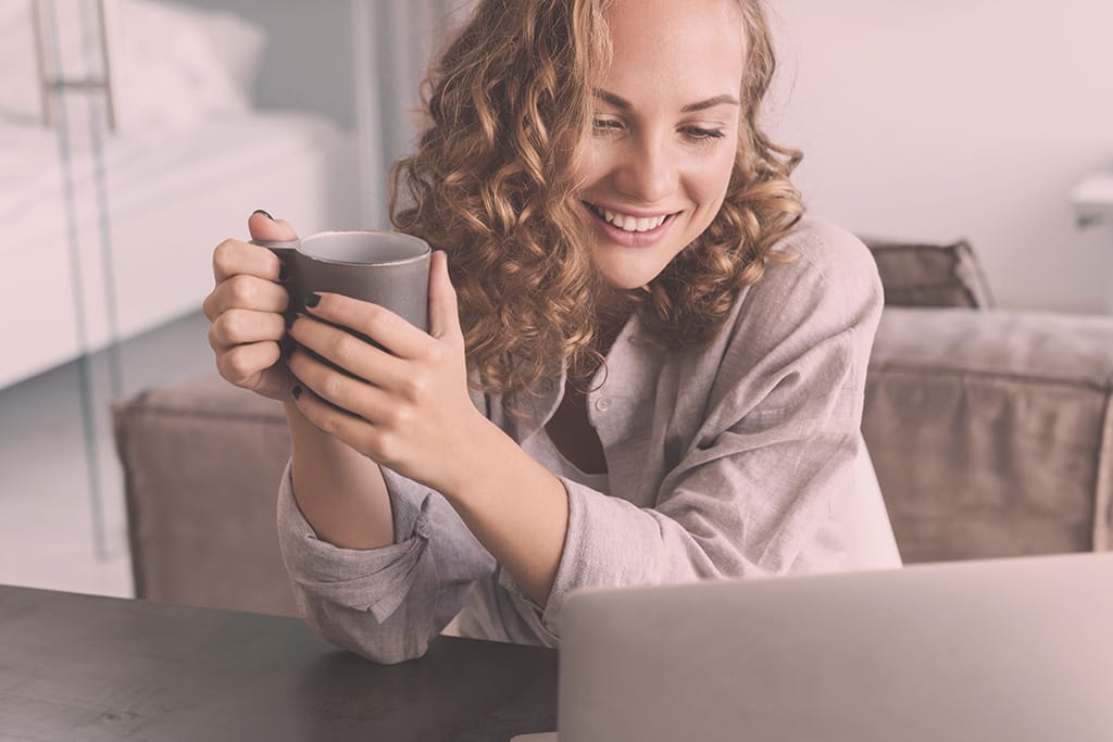 Smiling therapist holding a coffee cup while using a laptop